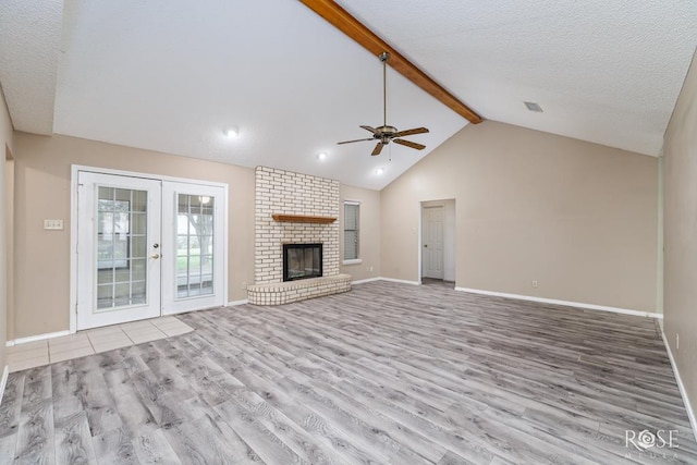 unfurnished living room with french doors, a brick fireplace, beam ceiling, and light wood-style floors