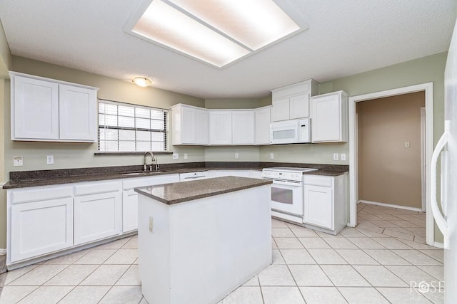 kitchen featuring dark countertops, white appliances, a kitchen island, and white cabinets