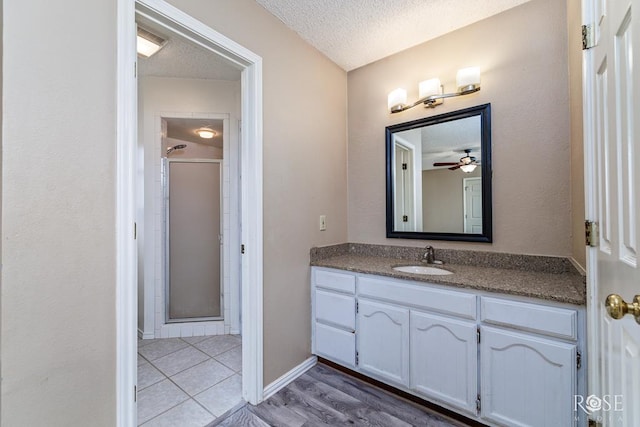 bathroom with a textured ceiling, vanity, baseboards, tile patterned floors, and a stall shower