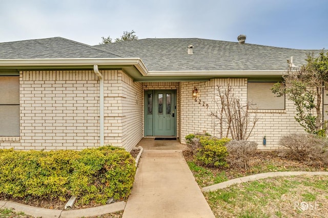 view of exterior entry with brick siding and roof with shingles