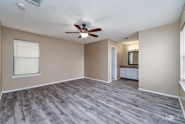 interior space featuring light wood finished floors, visible vents, ceiling fan, a sink, and baseboards