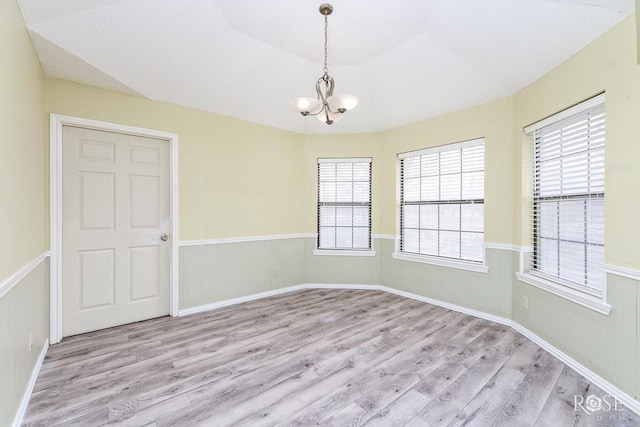 empty room featuring lofted ceiling, light wood-style floors, a chandelier, and wainscoting