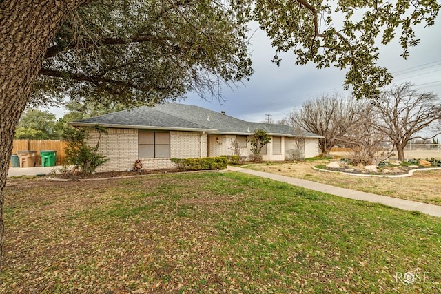 ranch-style house featuring a shingled roof, a front yard, fence, and brick siding