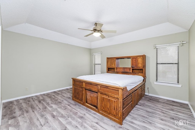 unfurnished bedroom with light wood-style floors, lofted ceiling, a textured ceiling, and baseboards