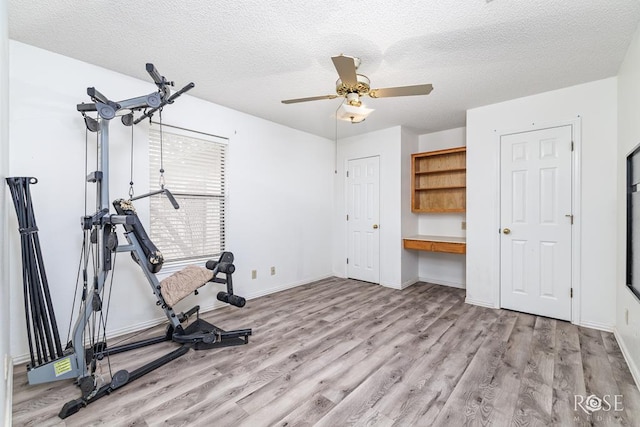 exercise room featuring a textured ceiling, light wood finished floors, built in study area, and baseboards