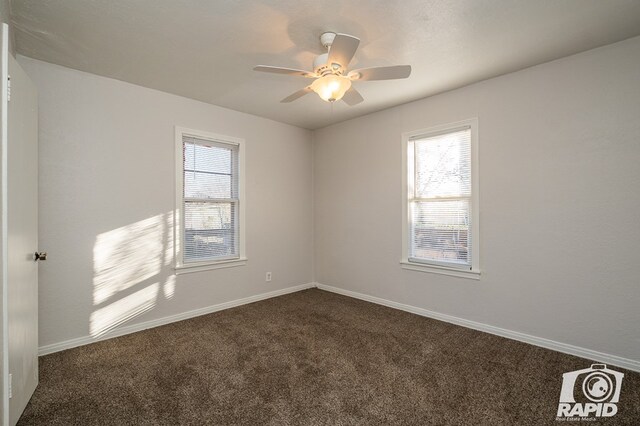 empty room with ceiling fan and dark carpet