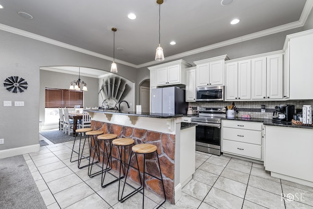 kitchen with white cabinetry, hanging light fixtures, a center island with sink, stainless steel appliances, and a kitchen bar