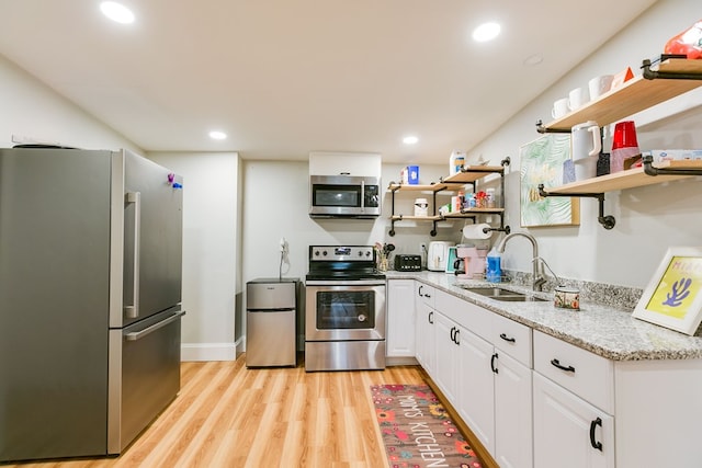 kitchen with sink, light hardwood / wood-style flooring, white cabinetry, stainless steel appliances, and light stone counters