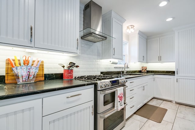 kitchen featuring sink, dark stone countertops, double oven range, white cabinets, and wall chimney exhaust hood