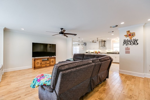 living room featuring crown molding, sink, light hardwood / wood-style flooring, and a wealth of natural light