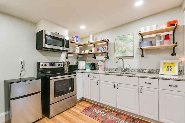 kitchen with sink, light stone counters, light hardwood / wood-style flooring, stainless steel appliances, and white cabinets