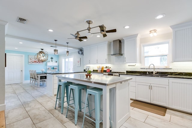 kitchen with white cabinetry, a kitchen island, sink, and wall chimney range hood