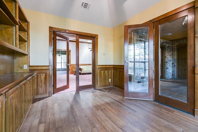  - doorway featuring french doors, wainscoting, wood finished floors, a textured ceiling, and vaulted ceiling