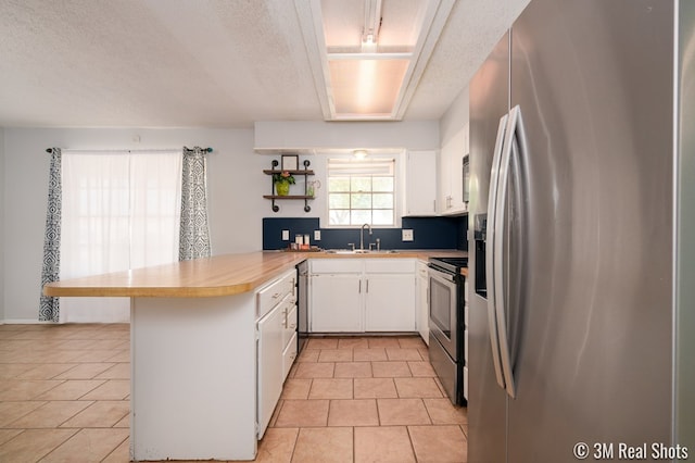 3317 Rockbrook Dr, San Angelo, TX 76904 - kitchen featuring stainless steel appliances, a peninsula, white cabinetry, light tile patterned floors, and a textured ceiling