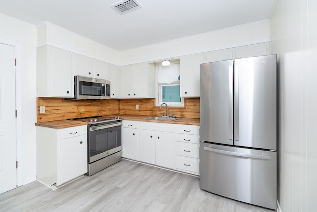 2007 Stanton St, Brady, TX 76825 - kitchen featuring stainless steel appliances, a sink, light wood finished floors, white cabinetry, and ornamental molding