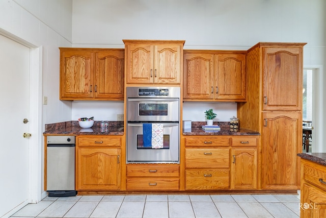 kitchen with stainless steel double oven, dark stone countertops, and light tile patterned floors