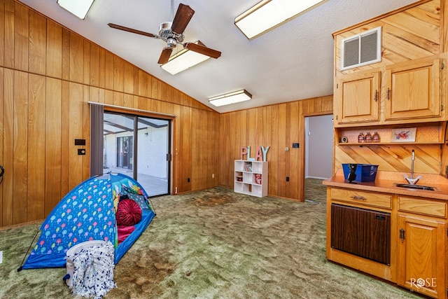 recreation room with vaulted ceiling, ceiling fan, carpet floors, and wood walls