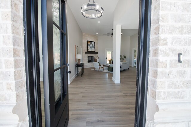 entrance foyer with a large fireplace, wood-type flooring, and ceiling fan with notable chandelier