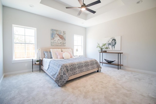 carpeted bedroom with a raised ceiling and ceiling fan