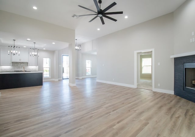 unfurnished living room with a high ceiling, ceiling fan with notable chandelier, a wealth of natural light, and light wood-type flooring