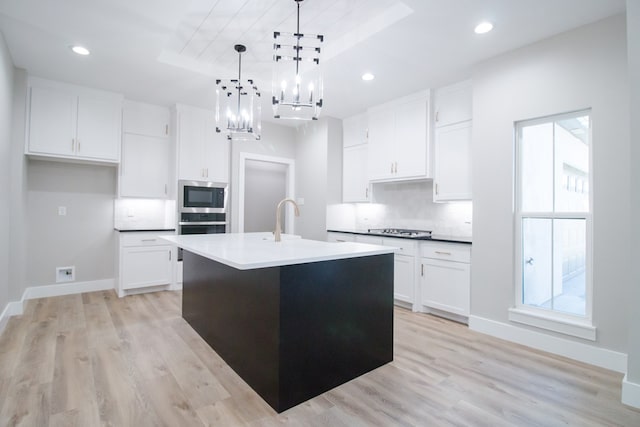 kitchen featuring stainless steel appliances, an island with sink, hanging light fixtures, and white cabinets