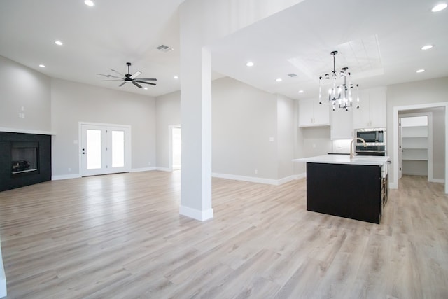 kitchen featuring light hardwood / wood-style flooring, white cabinetry, an island with sink, built in microwave, and decorative light fixtures