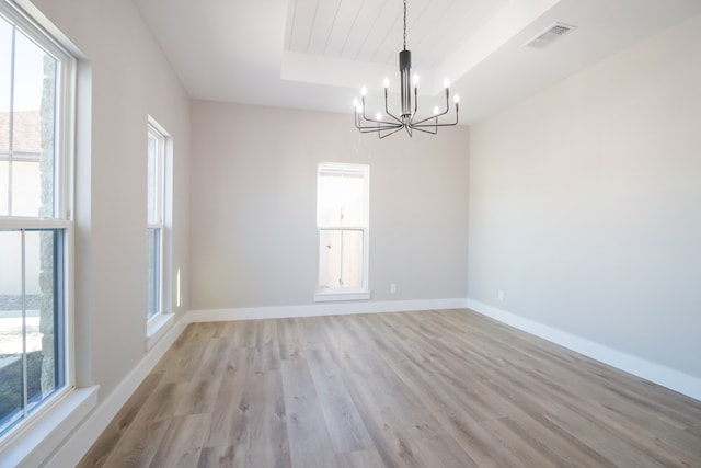 unfurnished room featuring a notable chandelier, a tray ceiling, and light wood-type flooring