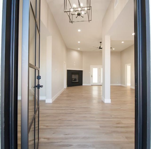 unfurnished living room with a towering ceiling, ceiling fan with notable chandelier, and light wood-type flooring