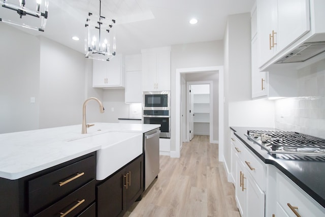 kitchen with stainless steel appliances, hanging light fixtures, a kitchen island with sink, and white cabinets