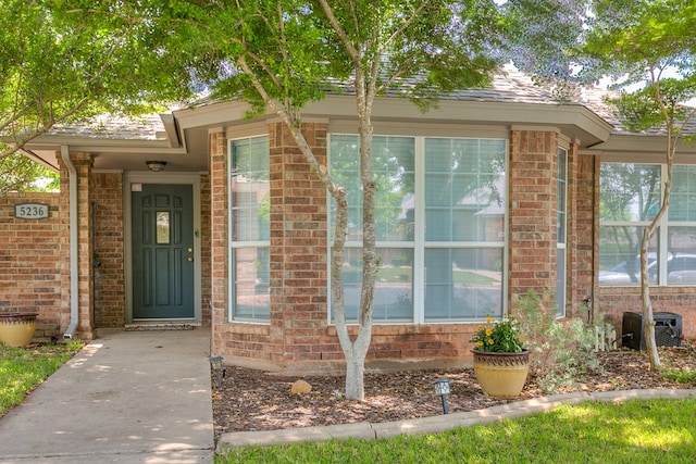 view of exterior entry featuring cooling unit and brick siding