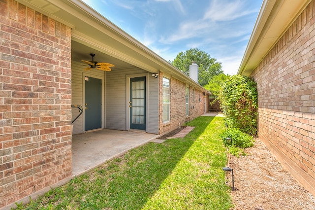 property entrance with a patio, a chimney, brick siding, a ceiling fan, and a lawn