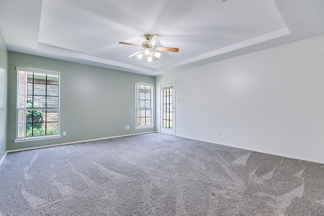 carpeted spare room featuring baseboards, ceiling fan, and a tray ceiling
