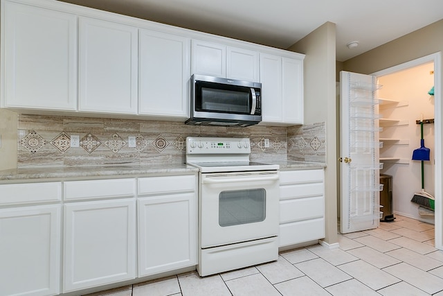 kitchen featuring white electric stove, tasteful backsplash, light tile patterned floors, stainless steel microwave, and white cabinetry