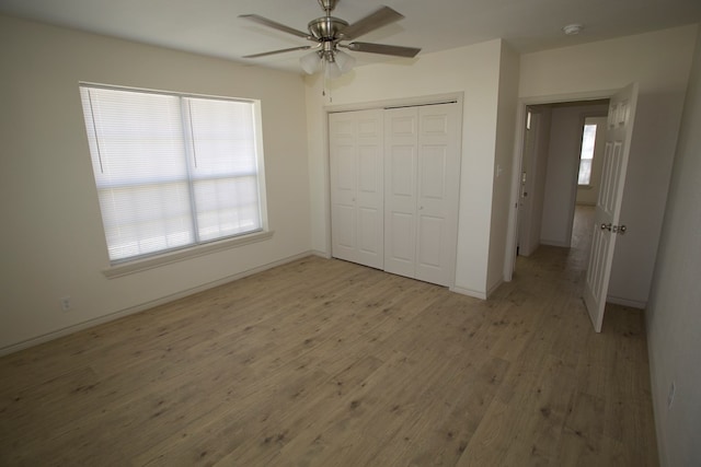 unfurnished bedroom with light wood-type flooring, a ceiling fan, baseboards, and a closet