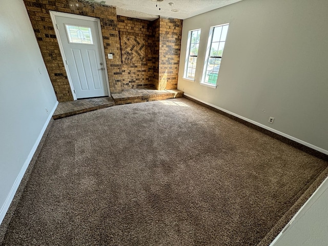 empty room featuring brick wall, carpet flooring, and a textured ceiling