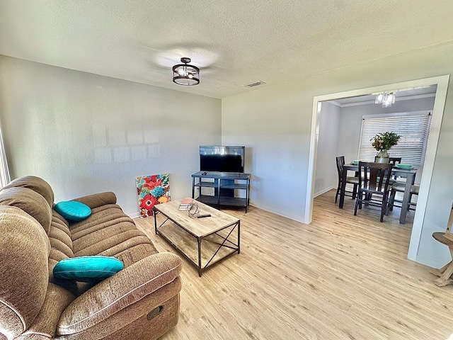 living room featuring a chandelier, light hardwood / wood-style floors, and a textured ceiling