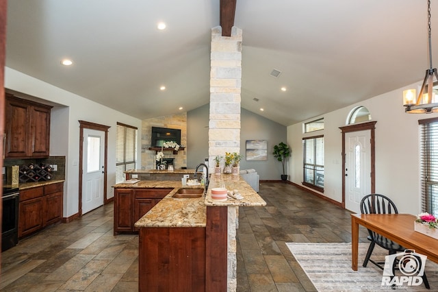 kitchen featuring sink, ornate columns, light stone counters, hanging light fixtures, and decorative backsplash