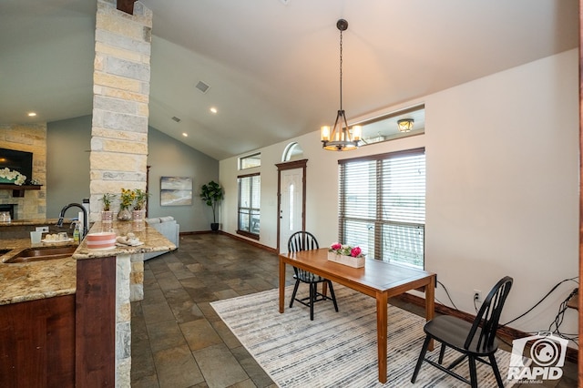 dining space with a stone fireplace, sink, high vaulted ceiling, and a chandelier