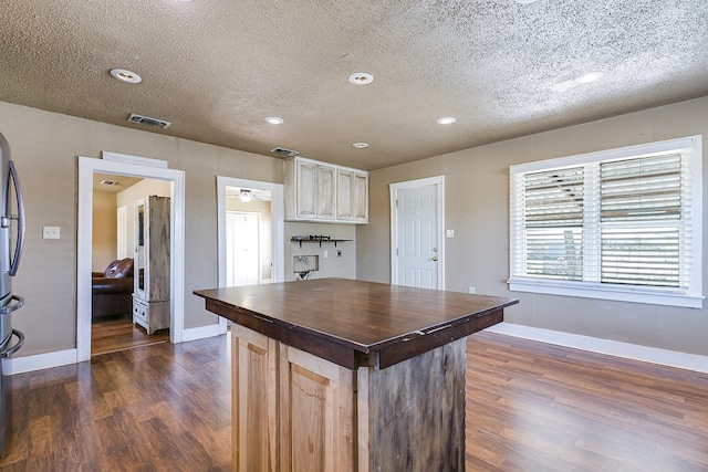 kitchen with stainless steel refrigerator, dark wood-type flooring, light brown cabinetry, and a textured ceiling