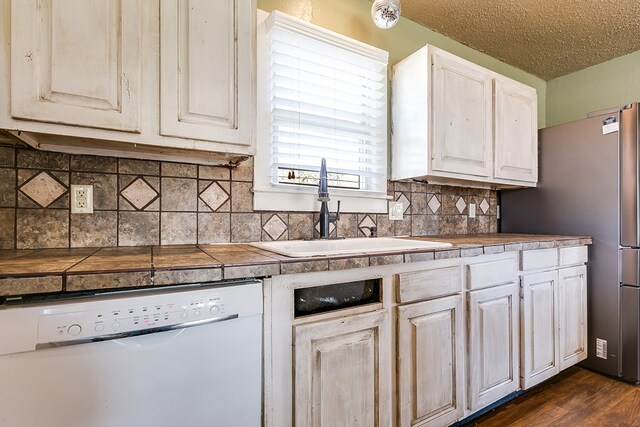 kitchen featuring sink, dishwasher, dark hardwood / wood-style floors, tile counters, and white cabinets