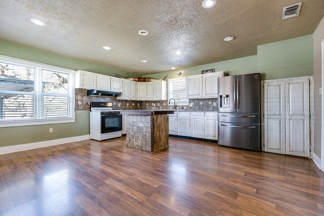 kitchen featuring gas range gas stove, backsplash, stainless steel refrigerator with ice dispenser, white cabinets, and a kitchen island