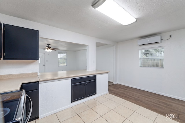 kitchen with a textured ceiling, light hardwood / wood-style flooring, a wall unit AC, range with electric cooktop, and ceiling fan