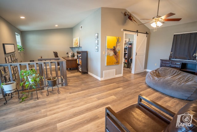 living room featuring lofted ceiling, light hardwood / wood-style flooring, a barn door, and ceiling fan