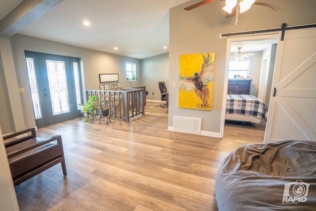 living area featuring vaulted ceiling, a barn door, and light hardwood / wood-style floors