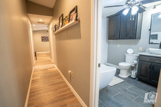 bathroom with ceiling fan, vanity, a bath, wood-type flooring, and toilet