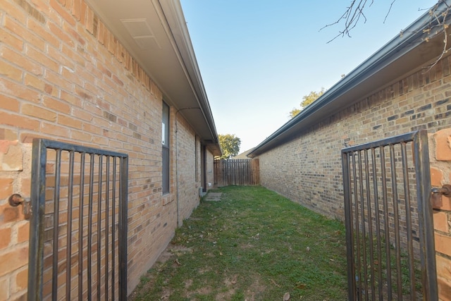 view of property exterior featuring brick siding, a lawn, and fence