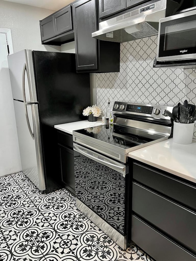 kitchen with under cabinet range hood, stainless steel appliances, tasteful backsplash, and light countertops