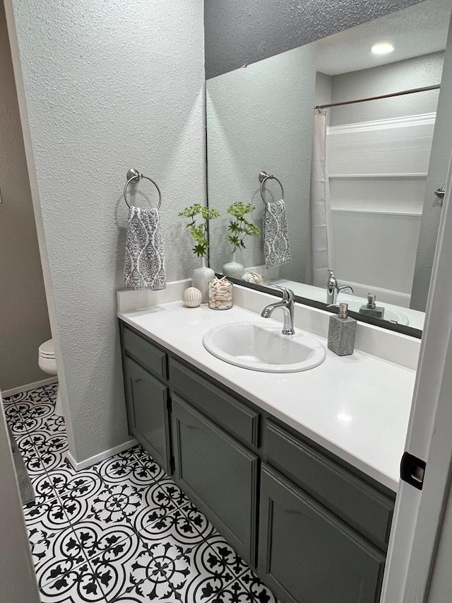 full bathroom with toilet, tile patterned flooring, baseboards, vanity, and a textured wall