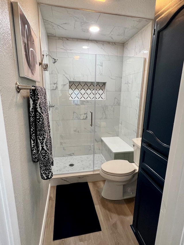 full bathroom with a stall shower, toilet, wood finished floors, and a textured wall