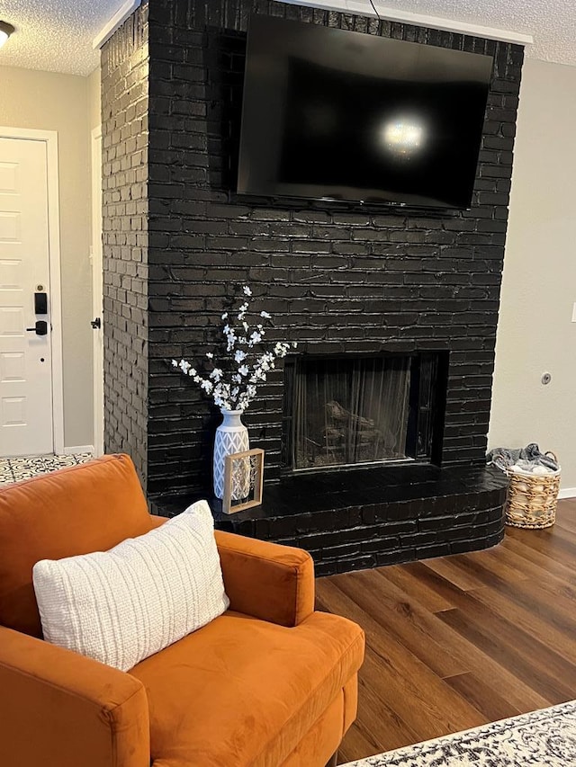 living area with baseboards, a textured ceiling, a brick fireplace, and wood finished floors